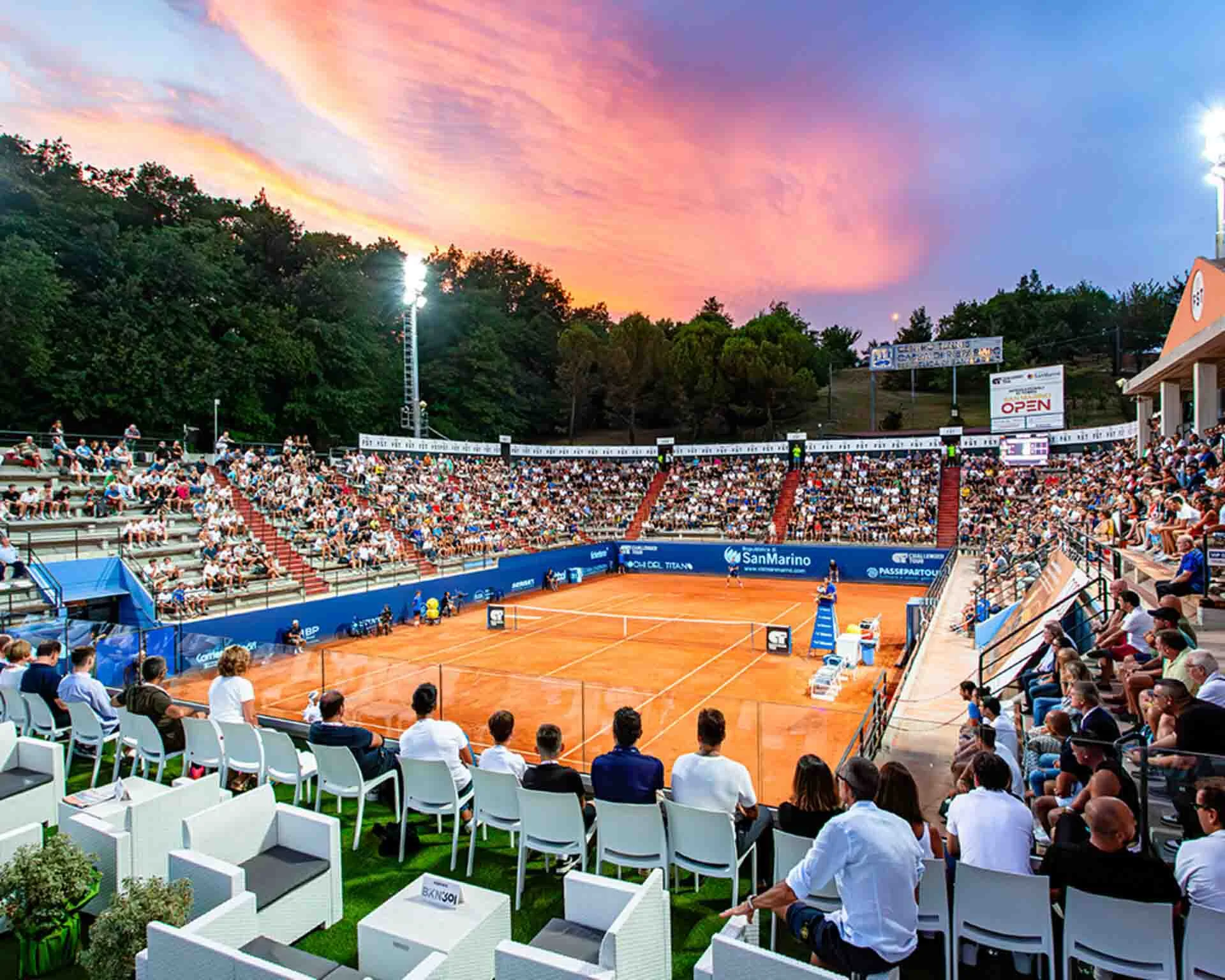 Wide angle shot of the ATP Challenger event San Marino Open, a full crowd at the centre court facility and an orange sunset in the sky